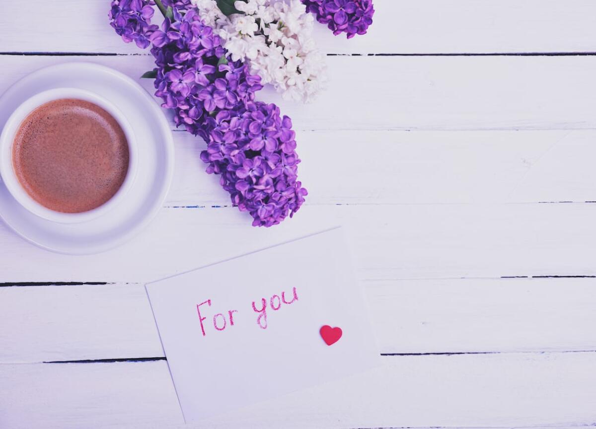 Lifestyle / Chi trova un lillà trova un amore... eterno - envelope with a sign for you on a white wooden surface, next to a cup of coffee, empty space on the right, vintage toning