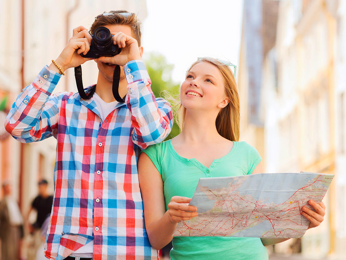 Estate 2024: i comportamenti da evitare quando si è in vacanza secondo gli italiani - travel, vacation, technology and friendship concept - smiling couple with map and photo camera exploring city