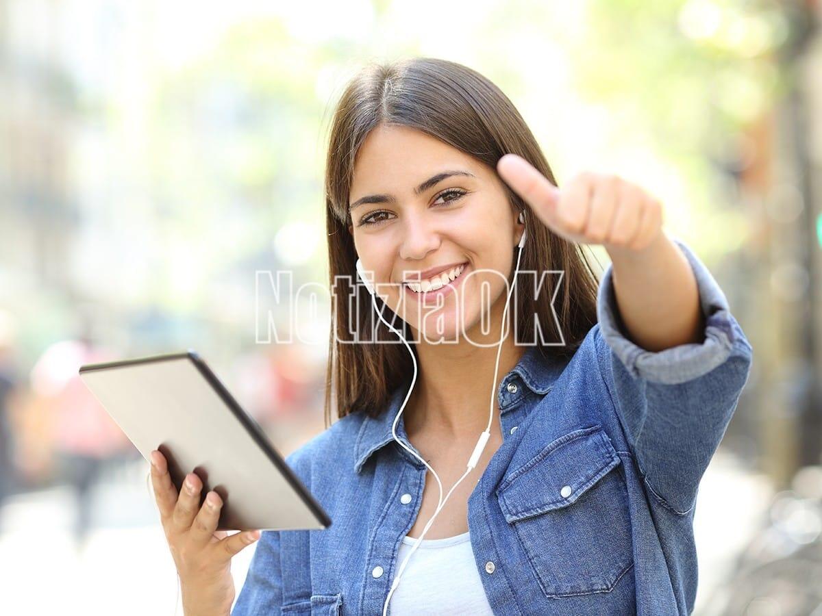 Lifestyle - Giovani pronti per le vacanze, ma quelle studio! - Happy teen listening to music holding a tablet with thumbs up in the street