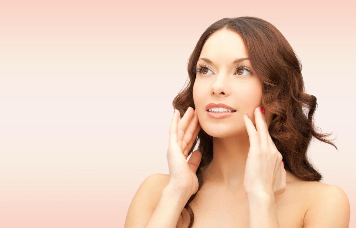 Lifestyle - Vitamine e idratazioni per una pelle in salute - beauty, people and health concept - beautiful young woman touching her face over pink background